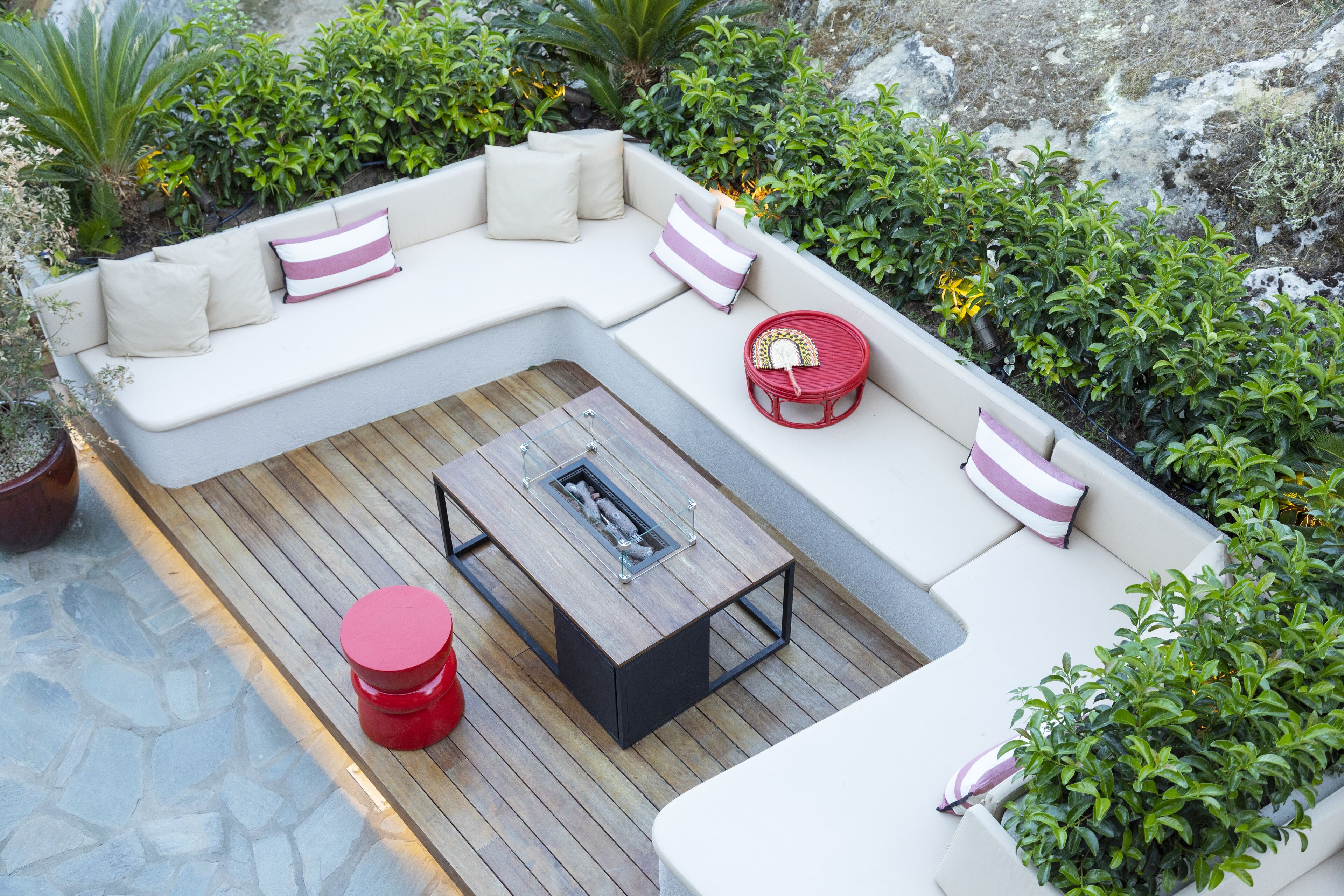 A modern outdoor seating area with a wooden table, cushioned seating, and a red chair.
