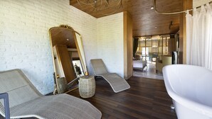 Ein Spa-Raum mit zwei Liegesesseln, einem großen Spiegel, einer weißen Badewanne und Holzböden.