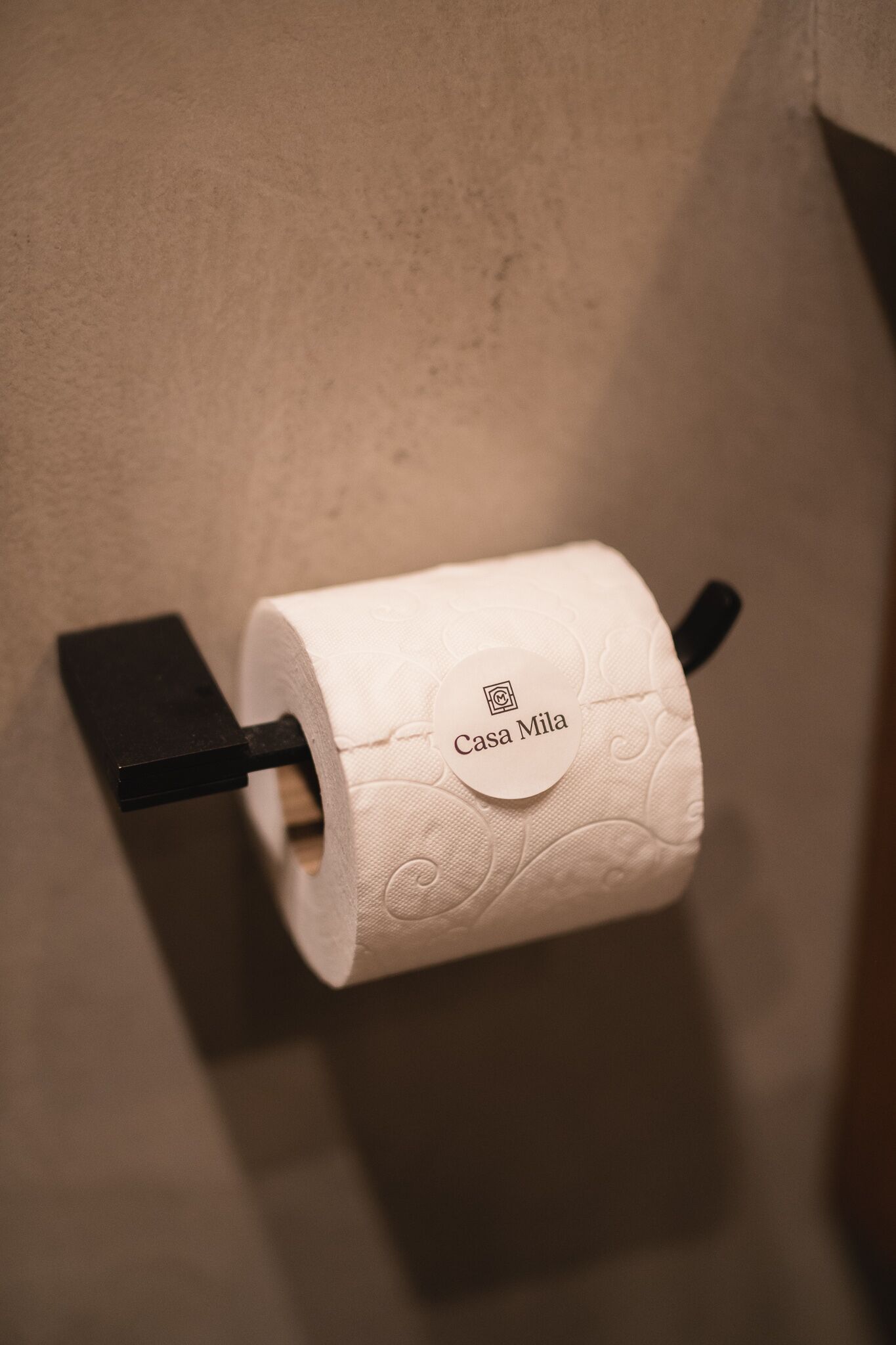 Toiletpapir monteret på en sort holder med en etiket med teksten 'Casa Mila'.