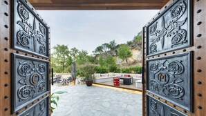 Un cancello aperto con decorazioni in metallo elaborate e un patio in pietra che conduce a un’area salotto esterna con tavoli e sedie.