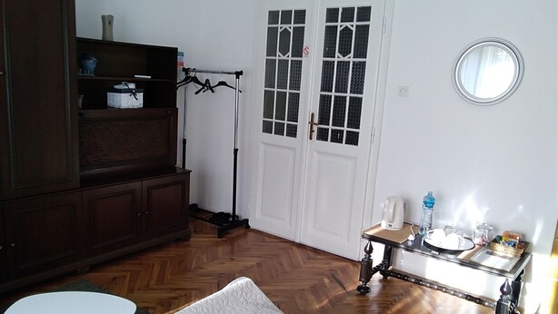 Une chambre d’hôtel comprenant un lit, une petite table avec une bouilloire et une bouteille d’eau, un miroir, une armoire et une porte avec une fenêtre.