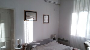 Une chambre à coucher comprenant un lit, deux lampes de chevet, une fenêtre avec des rideaux, un appareil de climatisation et une porte.