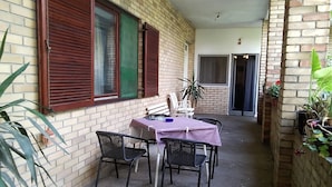 Une terrasse extérieure couverte, avec une table et des chaises, des murs en briques et des plantes en pot.