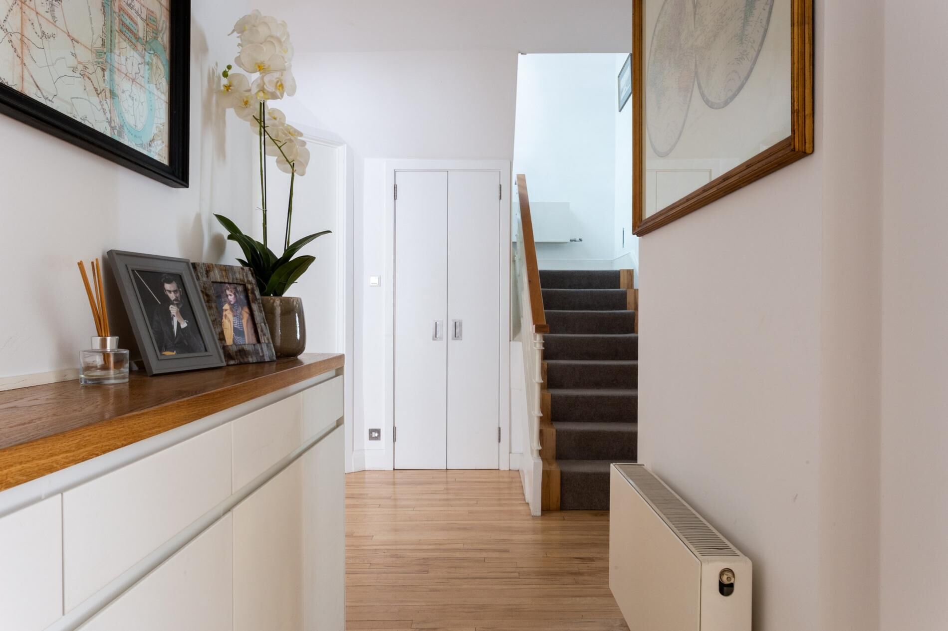 A hallway with a wooden counter, framed pictures, a potted plant, and a staircase leading to an upper floor.