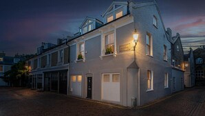A traditional building with a sign reading "Pembroke Mews." It features a corner entrance with a door, a small window with a plant, and a street lamp. - NEW Stunning 5BD Kensington House (London)