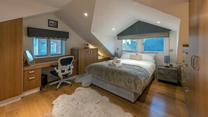 A bedroom with a sloped ceiling, a bed, a desk with a chair, a window, and a nightstand. - NEW Stunning 5BD Kensington House (London)