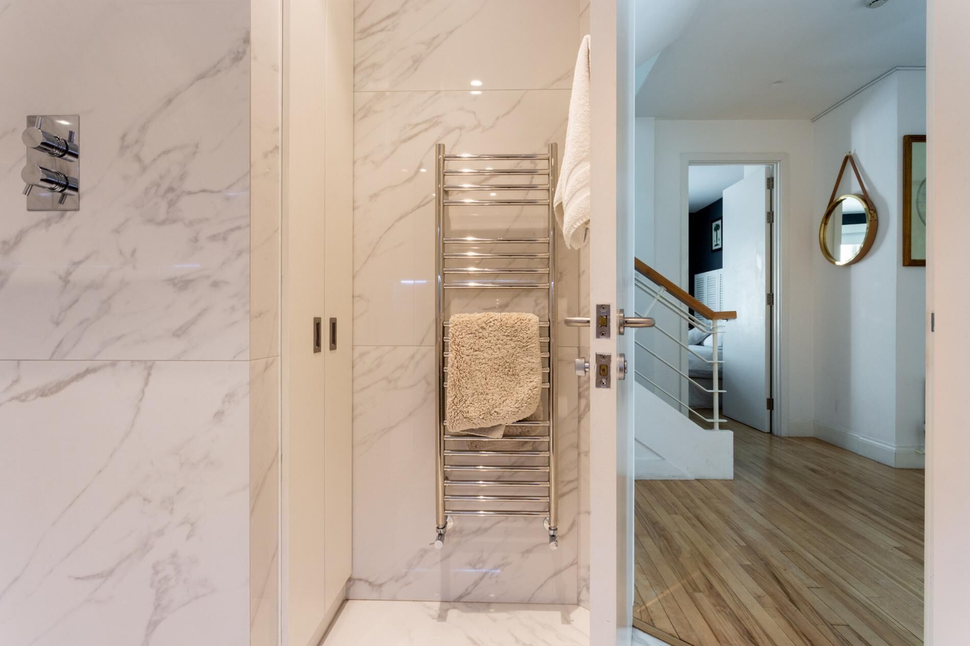 A bathroom with a marble wall, a towel rack with a towel, and a shower area.