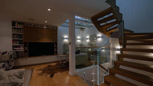 A modern living room with a flat-screen TV, wooden flooring, a sofa, and a staircase with glass railings. - NEW Stunning 5BD Kensington House (London)