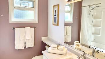 Un bagno con il water, lavandino e doccia. Asciugamani appesi al muro e un quadro incorniciato.
