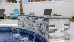 Ein Pool mit Wasserfall, umgeben von einer Steinmauer und einem weißen Zaun.