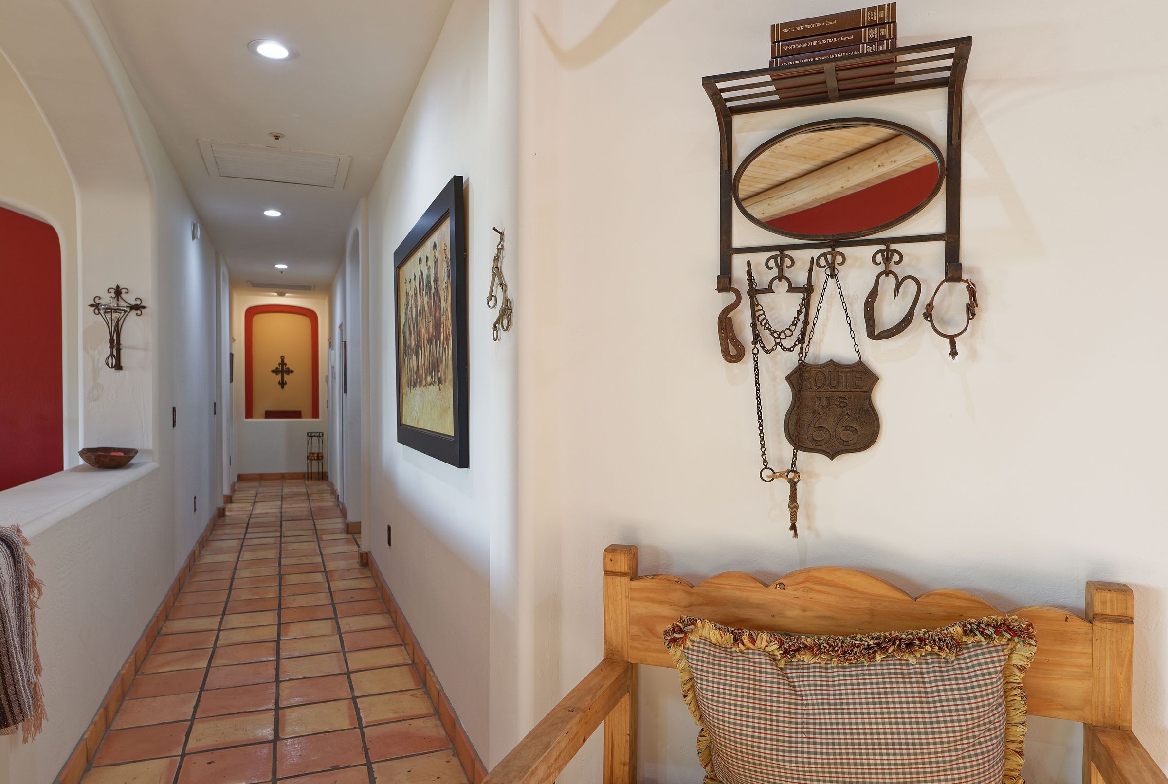 A hallway with a tiled floor, a wooden bench, a wall-mounted mirror, and various wall decorations including a framed picture and a Route 66 sign.