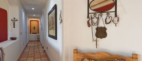 A hallway with a tiled floor, a wooden bench, a wall-mounted mirror, and various wall decorations including a framed picture and a Route 66 sign.