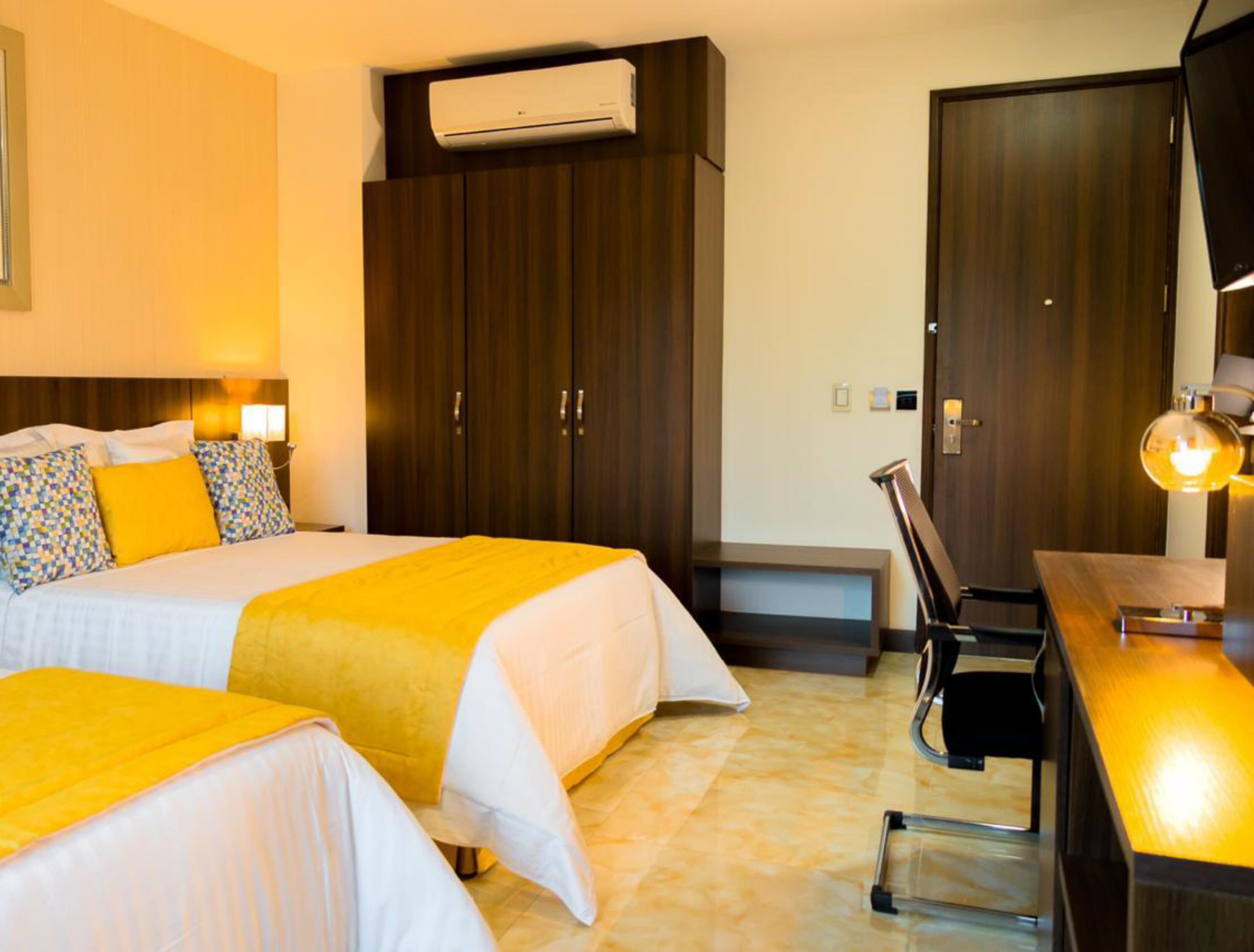 Une chambre d’hôtel avec deux lits, un bureau, une chaise, un appareil de climatisation et une armoire.