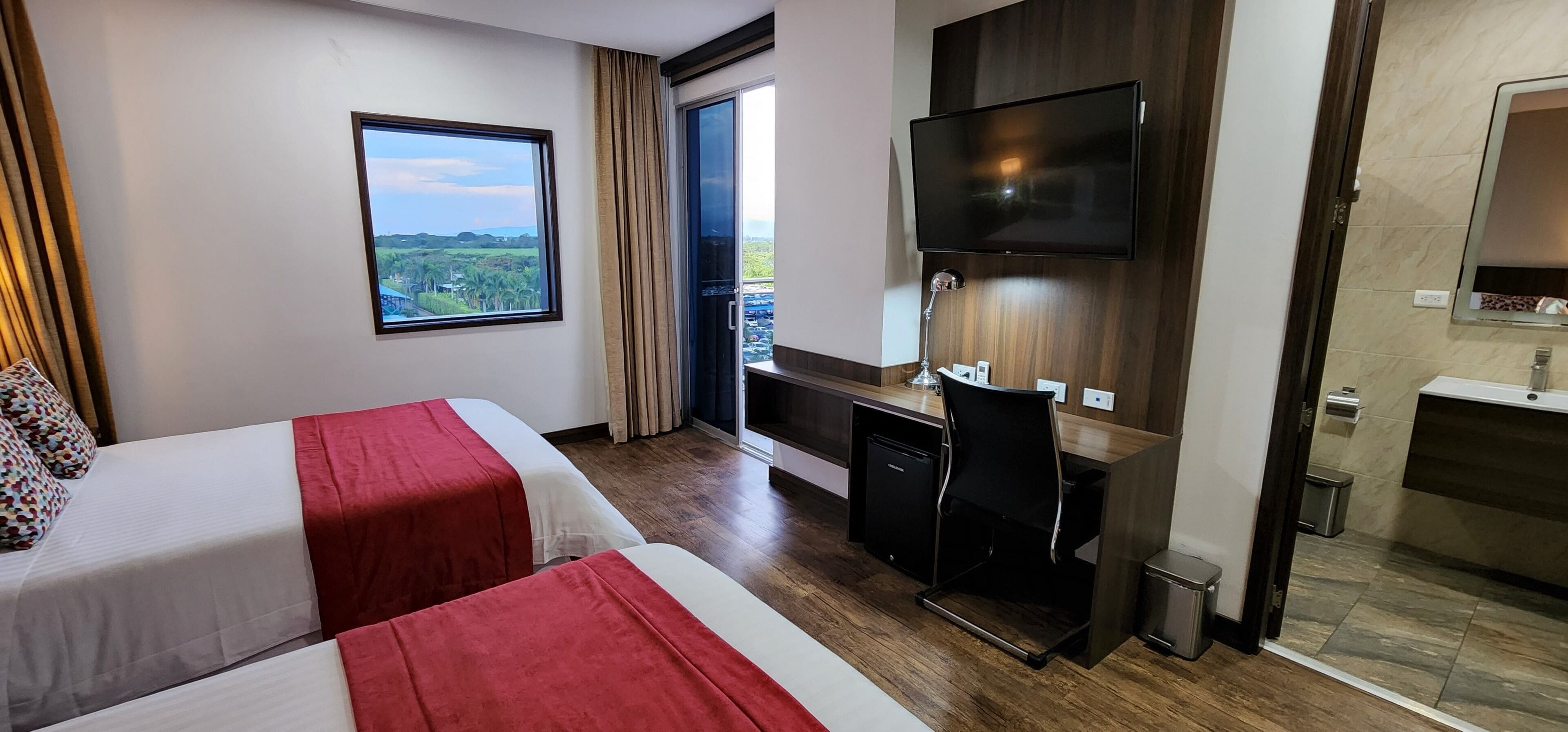 A hotel room with two beds, a desk, a TV, and a bathroom.