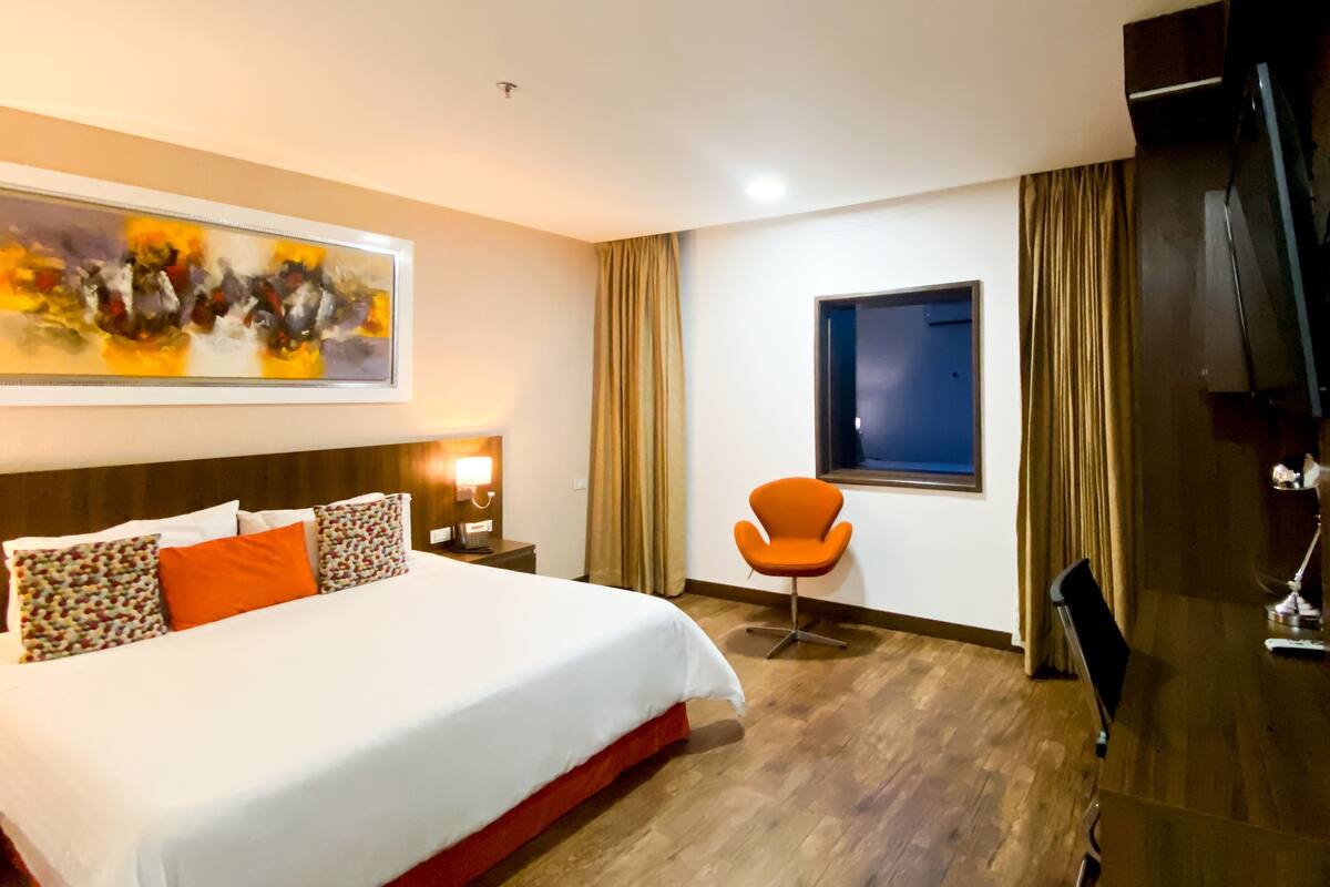 A hotel room with a large bed, a single chair, a TV, and a window.