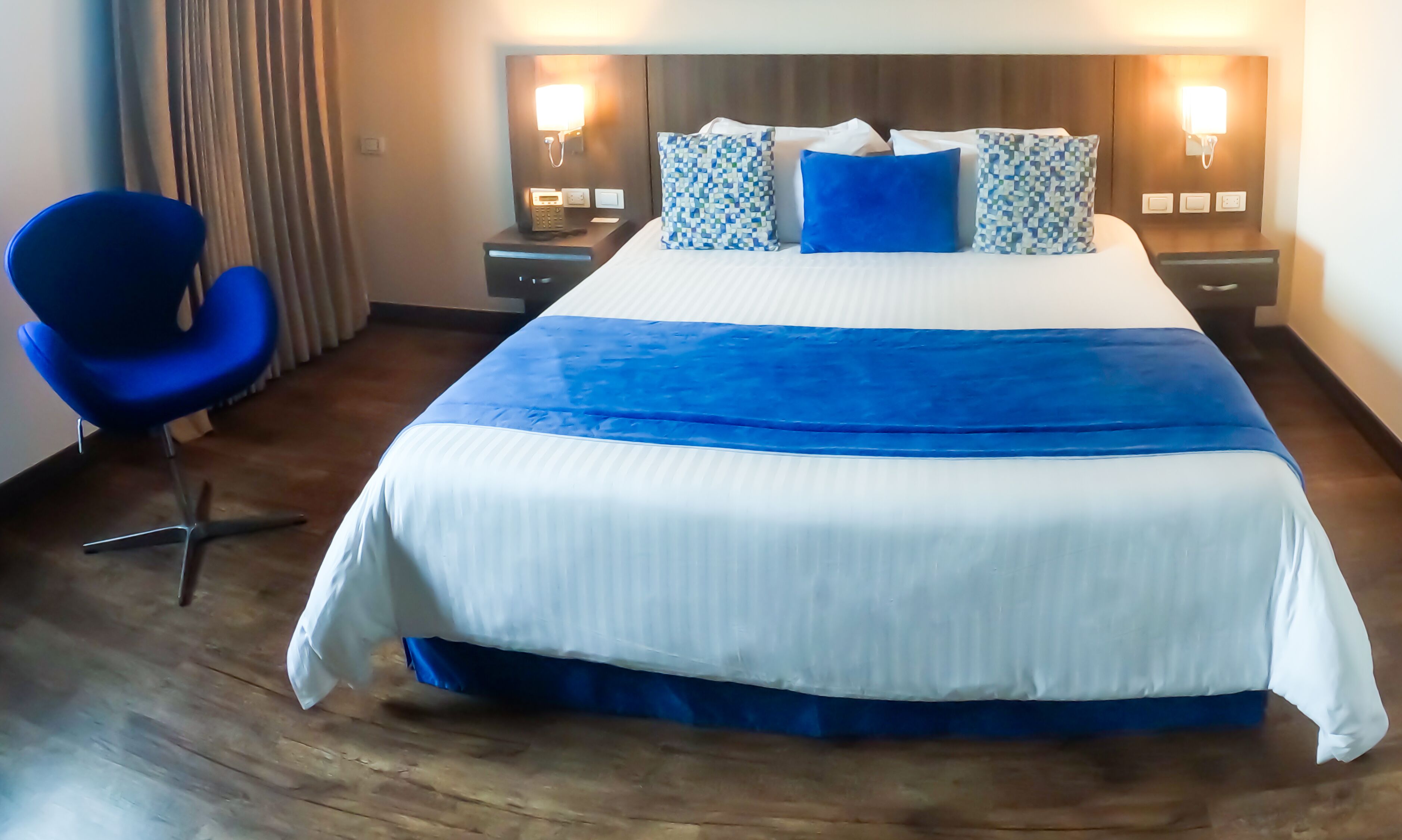 A hotel room with a large bed, a blue chair, and bedside lamps.