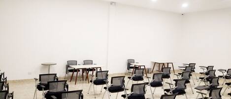 Una sala conferenze con file di sedie nere, un tavolo bianco e un tavolino rotondo.