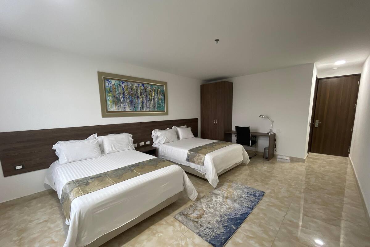 A hotel room with two beds, a desk, a chair, a wardrobe, and a painting on the wall.