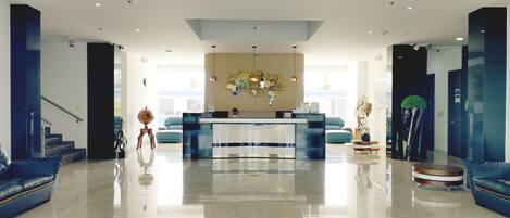 A spacious lobby with a reception desk, a staircase, and a large window providing natural light.