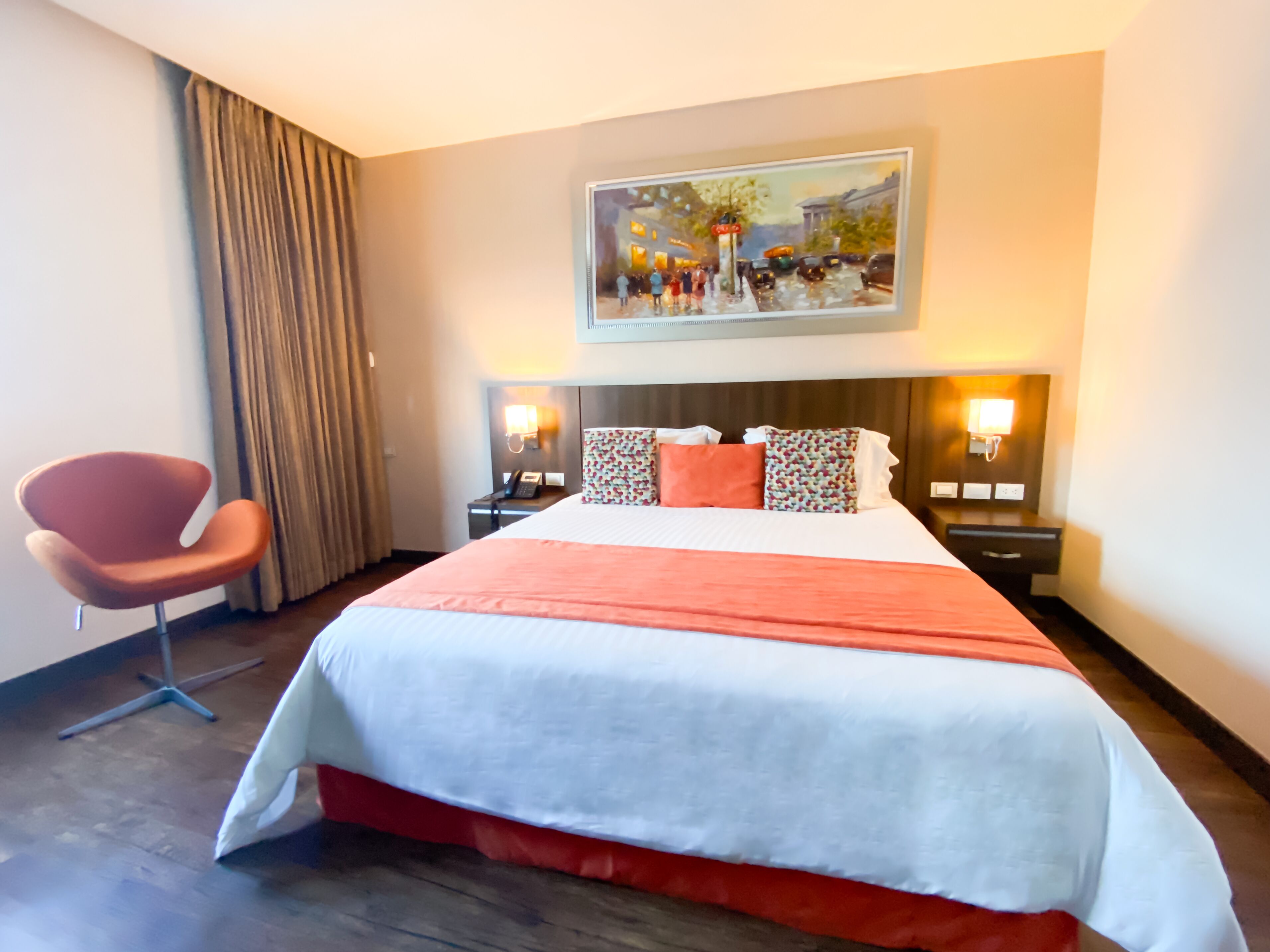Habitación de hotel con una cama grande, una silla, un cuadro en la pared y dos mesitas de noche con lámparas.