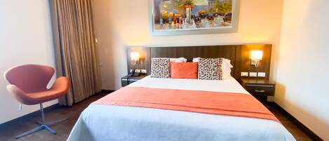 A hotel room with a large bed, a chair, a painting on the wall, and two bedside tables with lamps.