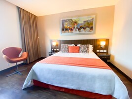 Habitación de hotel con una cama grande, una silla, un cuadro en la pared y dos mesitas de noche con lámparas.