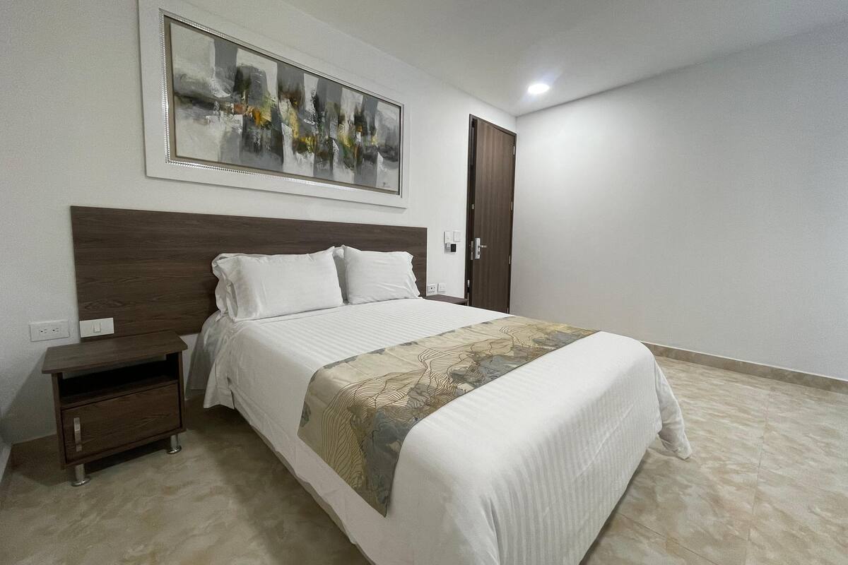 A bedroom with a bed, a nightstand, a wooden headboard, a door, and a painting on the wall.