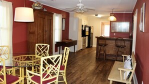 Cocina compacta con armarios de madera, un refrigerador y un comedor con sillas de mimbre y una mesa de vidrio.