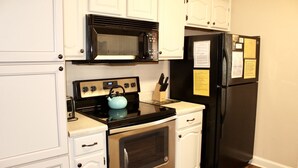 Una cocina con armarios blancos, un microondas negro, un refrigerador negro y un horno de acero inoxidable.