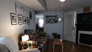 A living room with a sofa, a coffee table, and a fireplace. There are framed pictures on the wall and a clock. - Relaxing 2 bedroom river side home. Home located in Banner Elk, NC  (Banner Elk)
