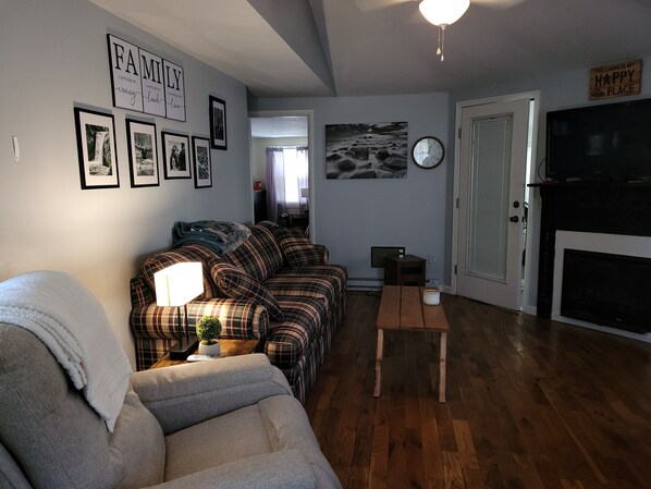 A living room with a sofa, a coffee table, and a fireplace. There are framed pictures on the wall and a clock. - Relaxing 2 bedroom river side home. Home located in Banner Elk, NC  (Banner Elk)