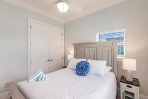 Un dormitorio con cama, mesita de noche, lámpara, ventana y ventilador de techo.