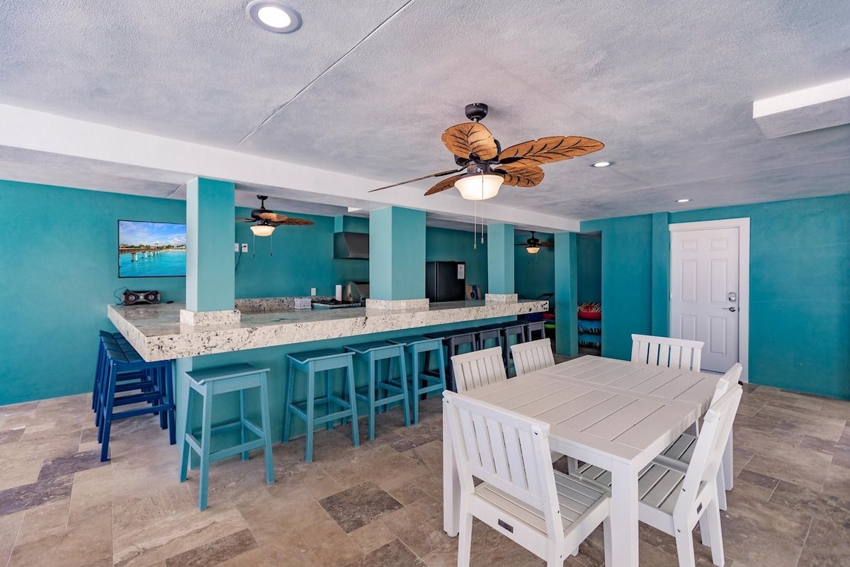 A kitchen with a bar area, a dining table with chairs, and a ceiling fan.
