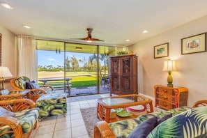 A spacious living room with wicker furniture, a glass door leading to a patio, and a ceiling fan. - Elegant Hawaiian Home ~ Residential Resort Living (Kahuku)
