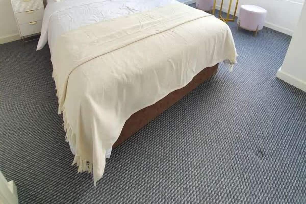 A bedroom with a large bed, two bedside tables, a window, and a view of buildings outside.