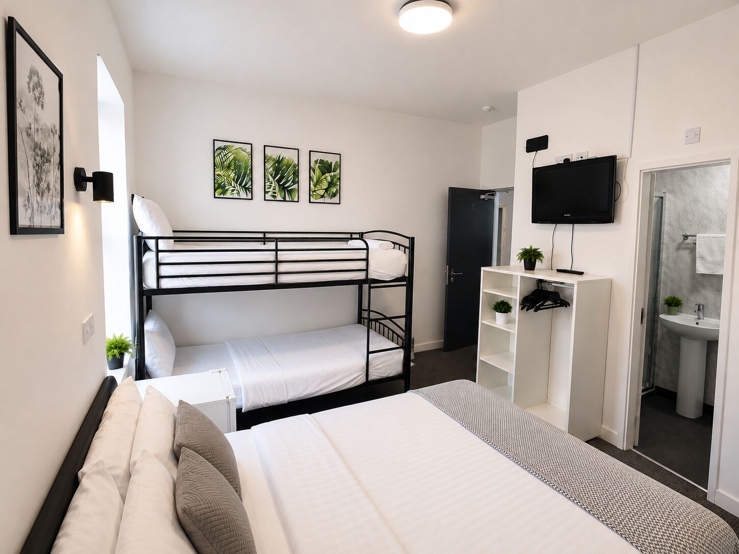 A bunk bed room with a desk, TV, and a bathroom with a mirror and sink.