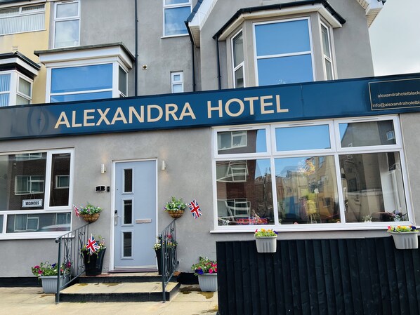 Exterior del Hotel Alexandra con un letrero, una puerta, ventanas y plantas en macetas.