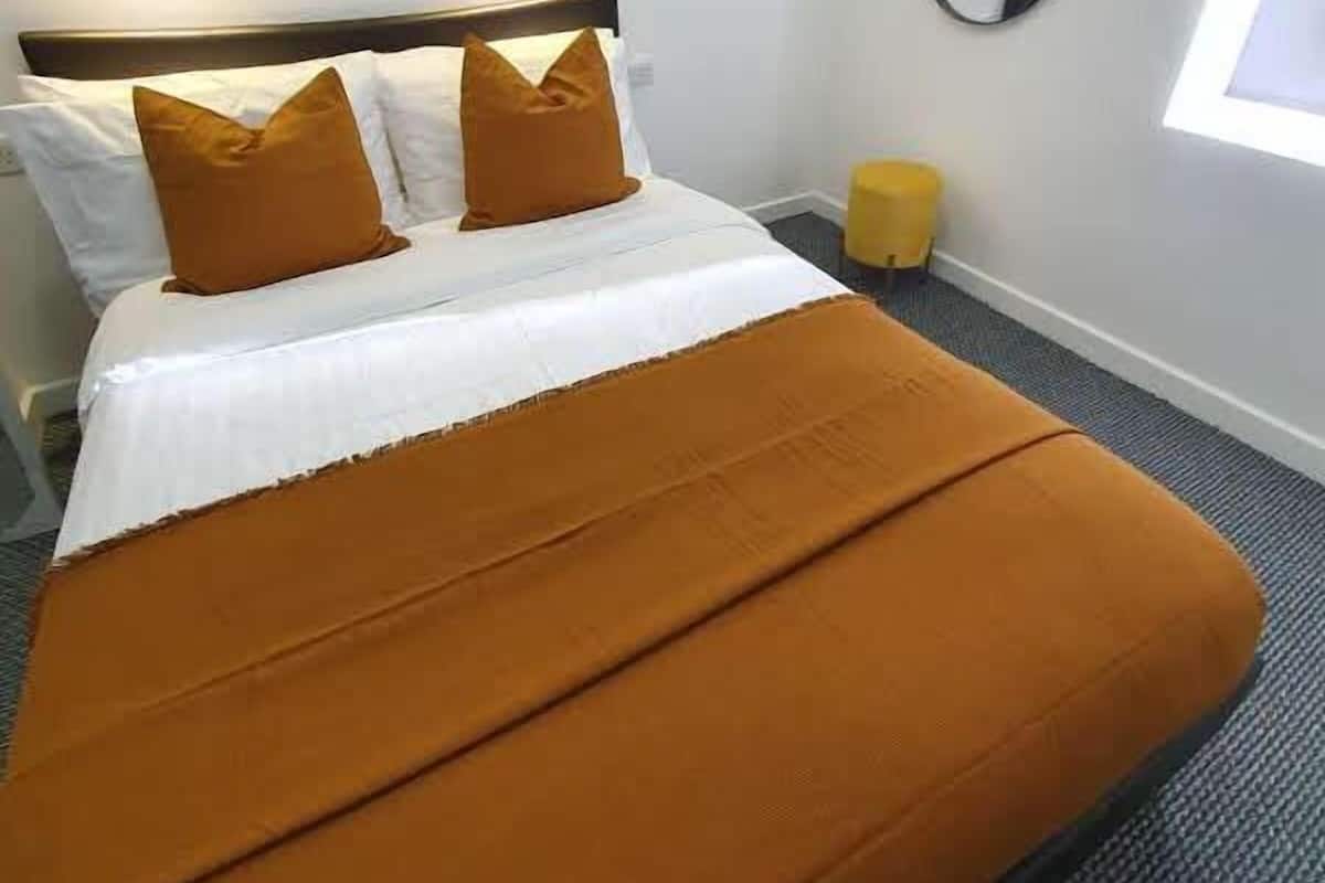 A hotel room with a bed, two pillows, a bedside lamp, a round mirror, and a window.
