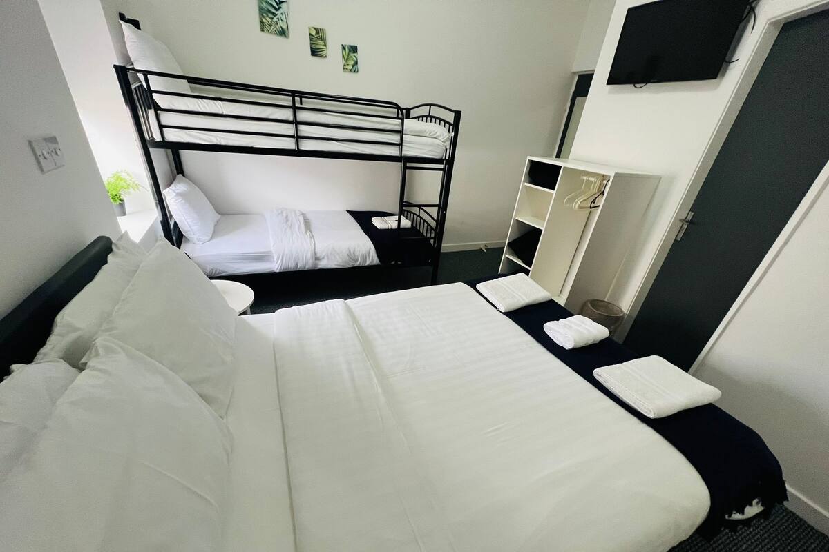 A hotel room with two bunk beds, a small desk, a chair, a TV mounted on the wall, and a door.