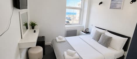 Habitación de hotel con cama, mesita de noche, televisor, ventana con vistas y una pequeña planta en maceta.