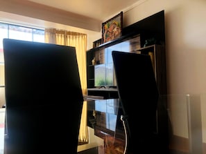 A room with a TV mounted on the wall, a chair in the foreground, and a window with curtains. - Departamento Alice (Cusco)
