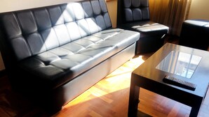 A modern living room with a black leather sofa, a matching armchair, and a glass coffee table. - Departamento Alice (Cusco)