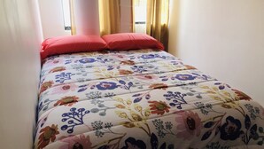 A bed with a floral-patterned bedspread and two red pillows. - Departamento Alice (Cusco)