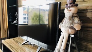 A doll sitting on a stool next to a flat-screen TV on a wooden floor. - Departamento Alice (Cusco)