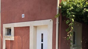 Un bâtiment rouge avec une porte blanche, une petite fenêtre et un paillasson.