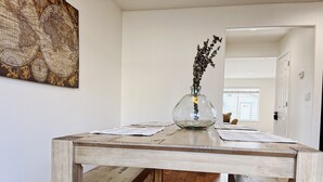 Une table à manger en bois, ornée d’un vase de fleurs séchées, une carte accrochée au mur et un plancher en bois.