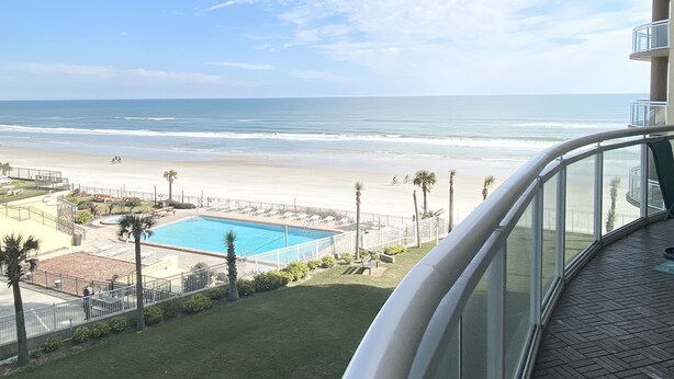Ein Balkon mit Blick auf einen Strand, ein Schwimmbad und einen klaren Himmel.