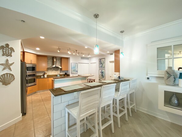 A modern kitchen with a central island, white bar stools, and a dining area.