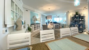 Ein geräumiges Wohnzimmer mit Essbereich, ausgestattet mit weißen Möbeln, einer blauen Akzentwand und einem dekorativen Regal mit Stranddekoration.