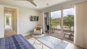 Een moderne slaapkamer met een bed, een plafondventilator, een televisie en een balkon met buitenmeubilair.